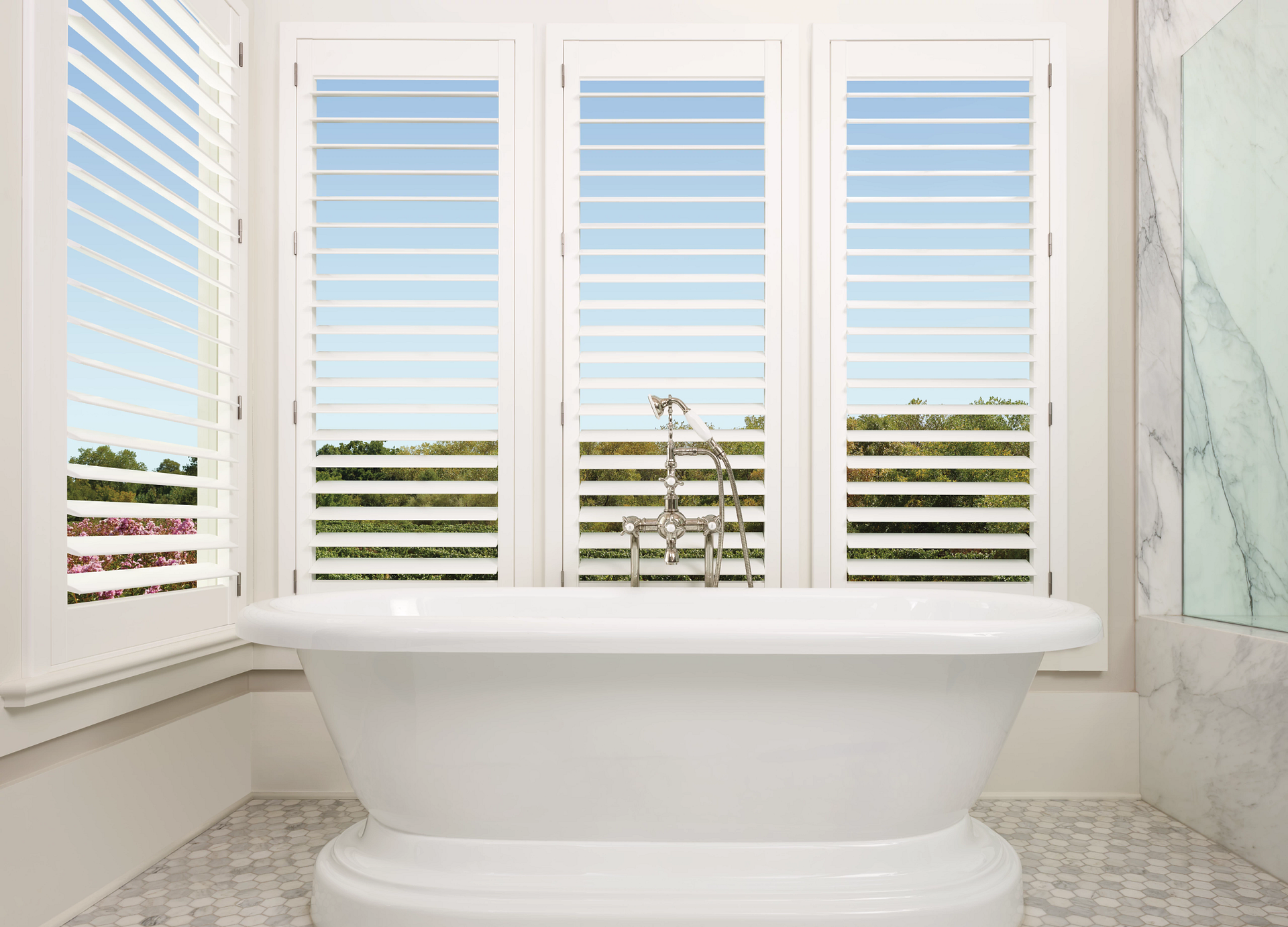 Open Hunter Douglas Palm Beach™ Polysatin™ Vinyl Shutters in a white bathroom with a stand-alone tub