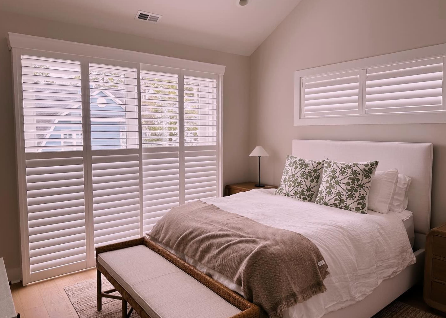 Bedroom with white shutters, bed, bench, and neutral decor.