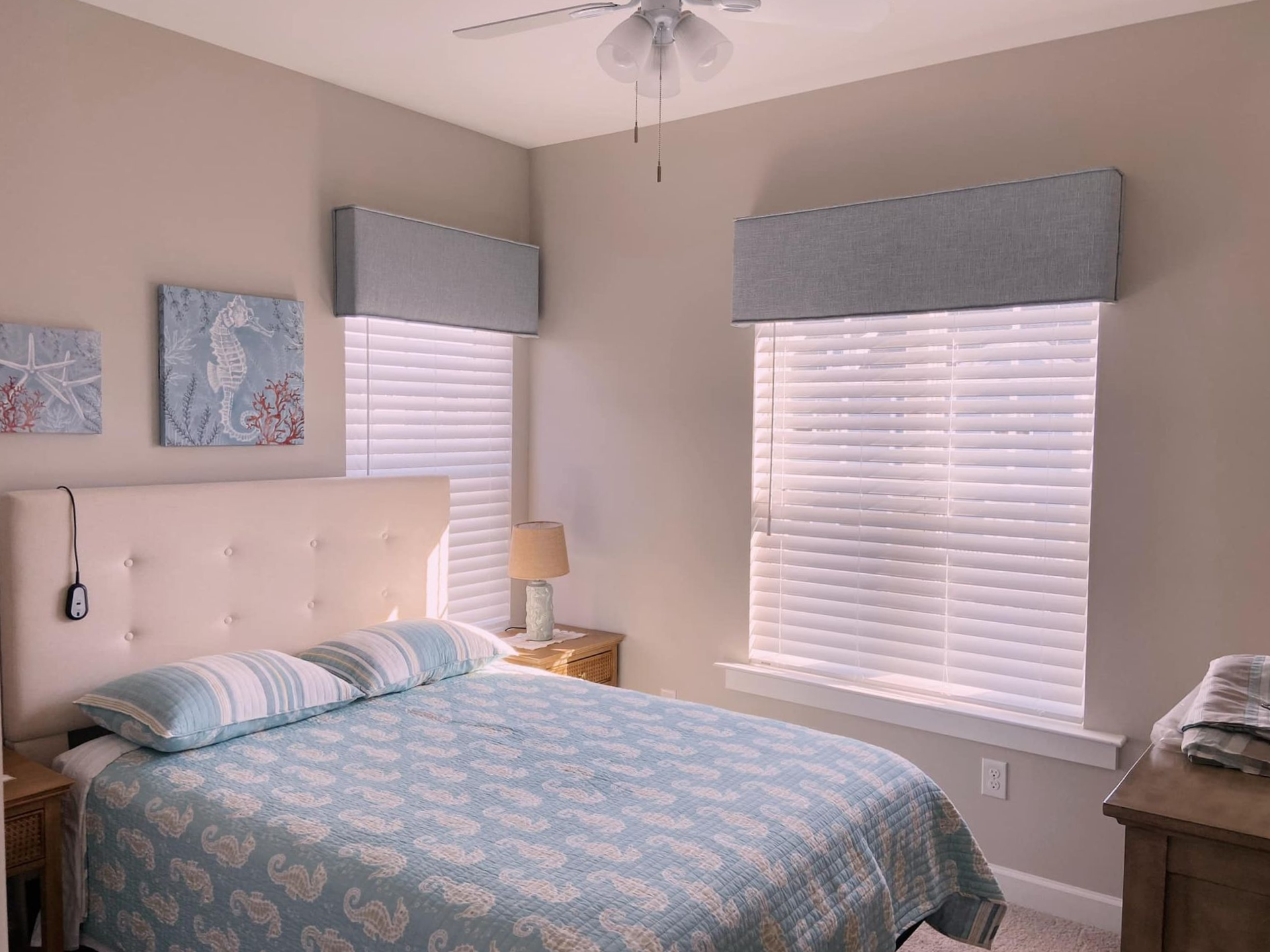 Bedroom with a bed, two windows, light blue and beige color scheme, and beach themed art.