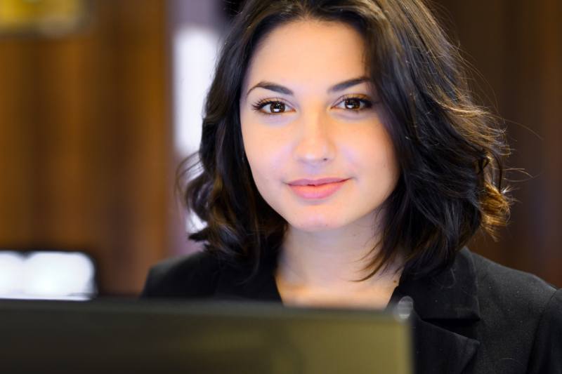Woman with dark bob, looking at a computer screen, wearing a black blazer, indoors.