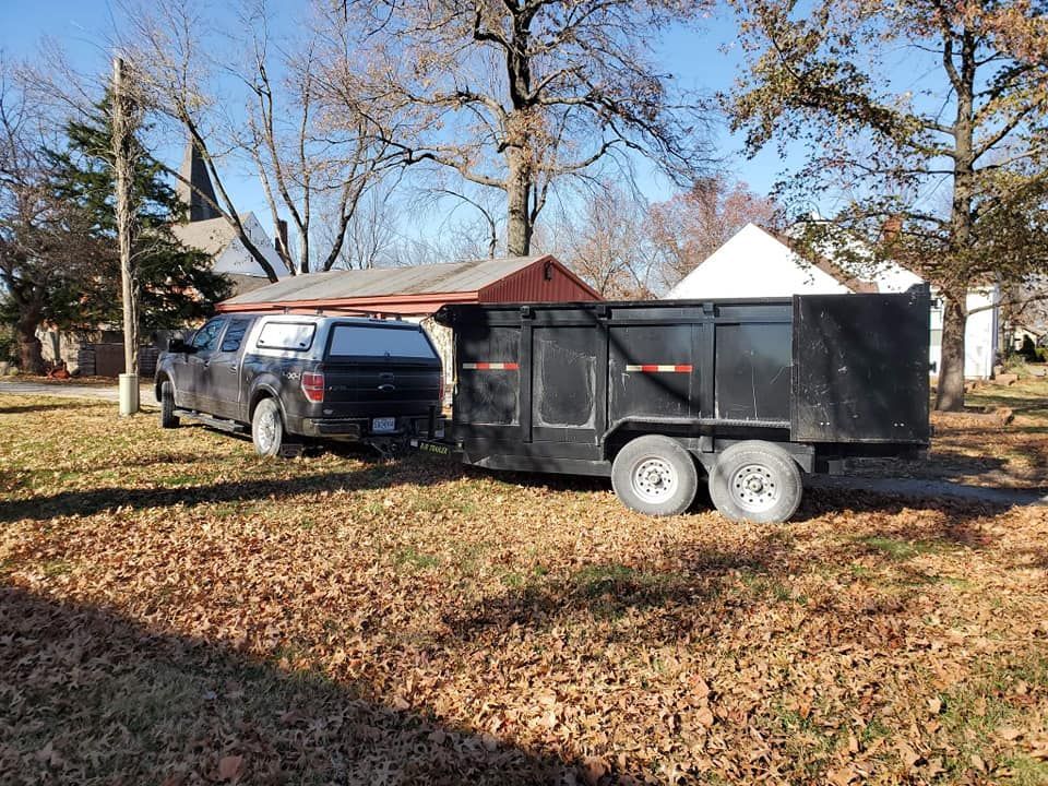 A truck is towing a dumpster trailer in a yard.