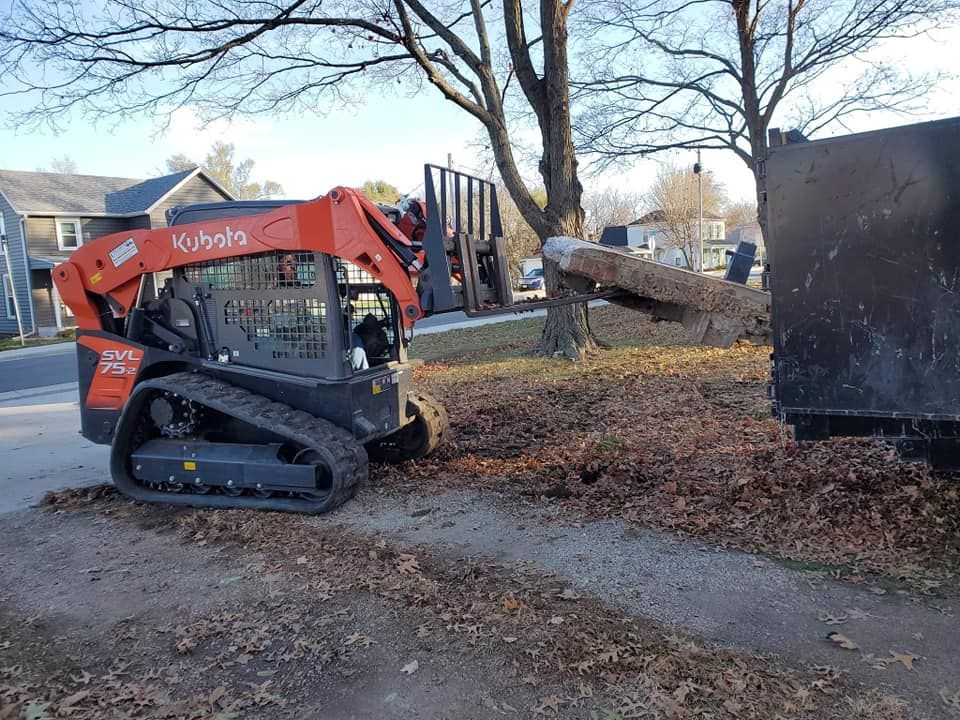 A kubota skid steer is parked on the side of the road next to a dumpster.