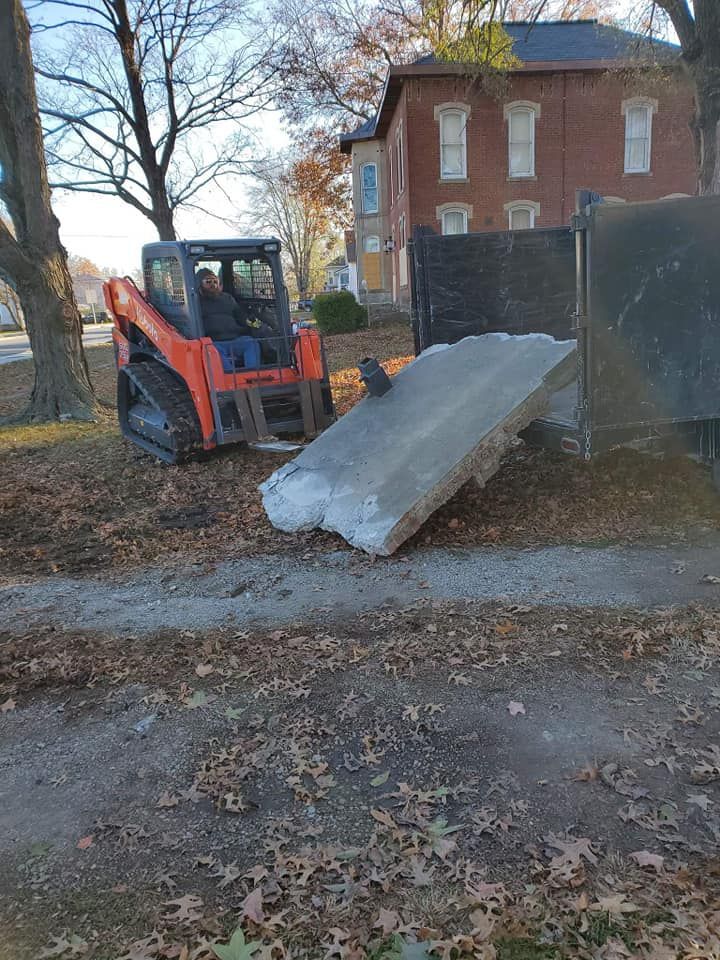 A bulldozer is loading a large concrete slab into a dumpster.