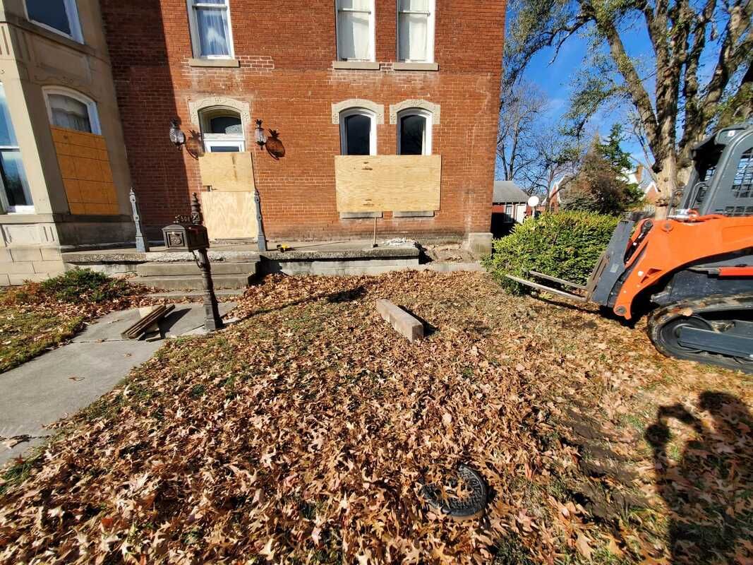 A bulldozer is sitting in front of a brick building covered in leaves.