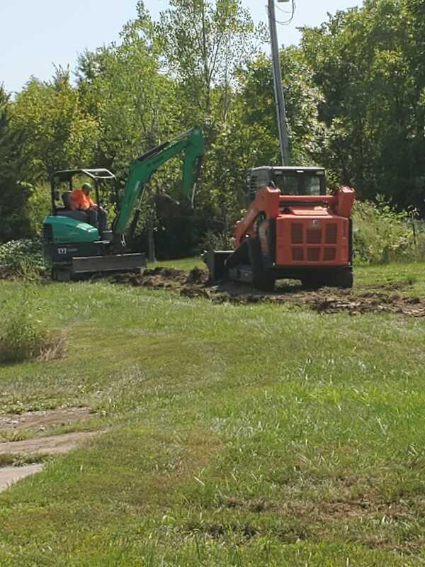 A man is driving an excavator in a grassy field