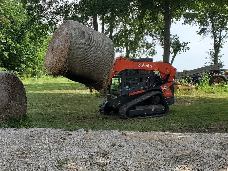 A bulldozer is carrying a bale of hay in a field.