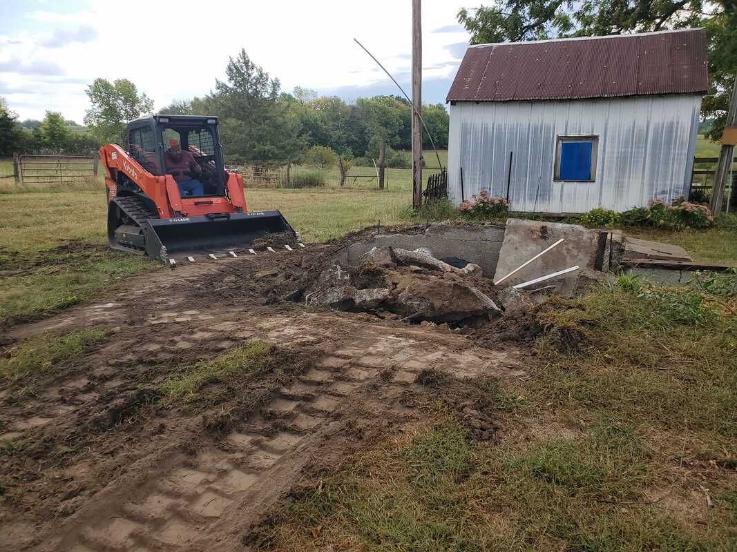 A man is driving a bulldozer in a field in front of a white building.