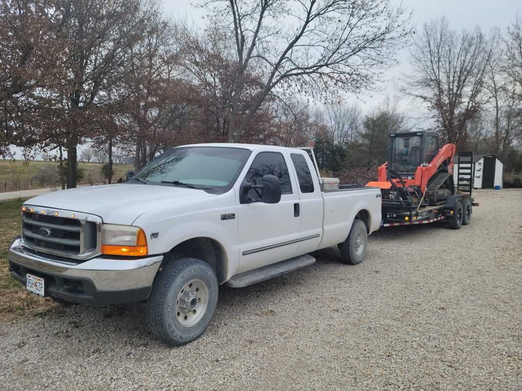 A white truck is towing a trailer with a tractor on it.