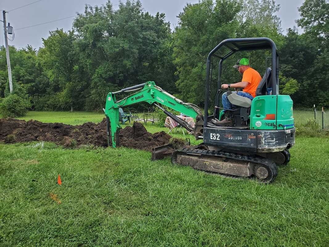 A man is driving a green excavator in a grassy field.