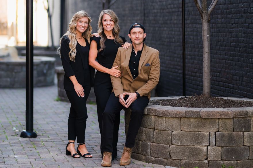 A man and two women are posing for a picture while sitting on a stone wall.