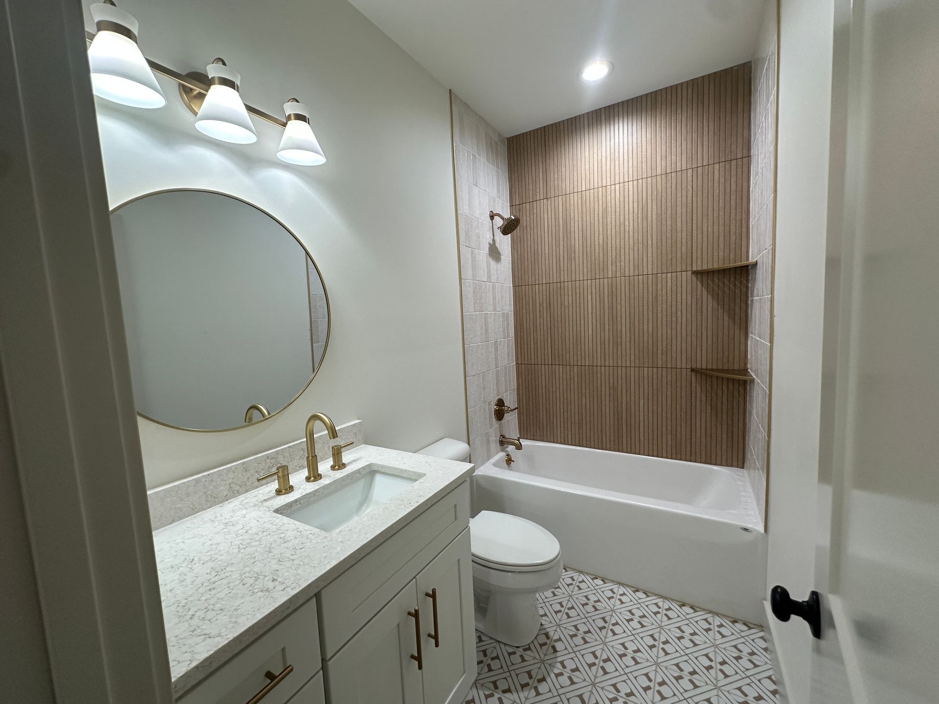 Bathroom with a wood-look accent wall, white vanity, round mirror, and patterned floor tiles.