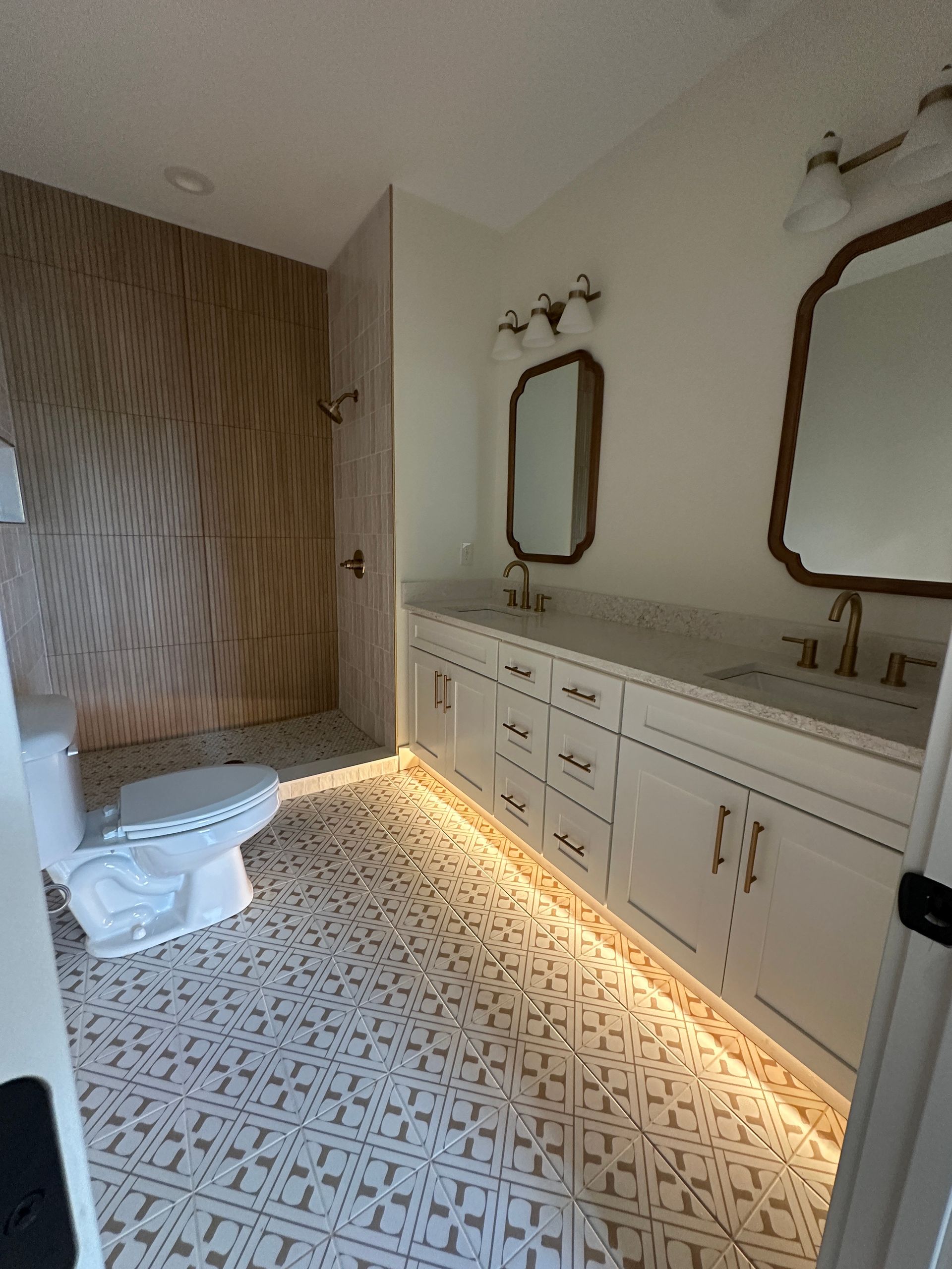 Bathroom with white cabinets, patterned floor, shower, and under-cabinet lighting.