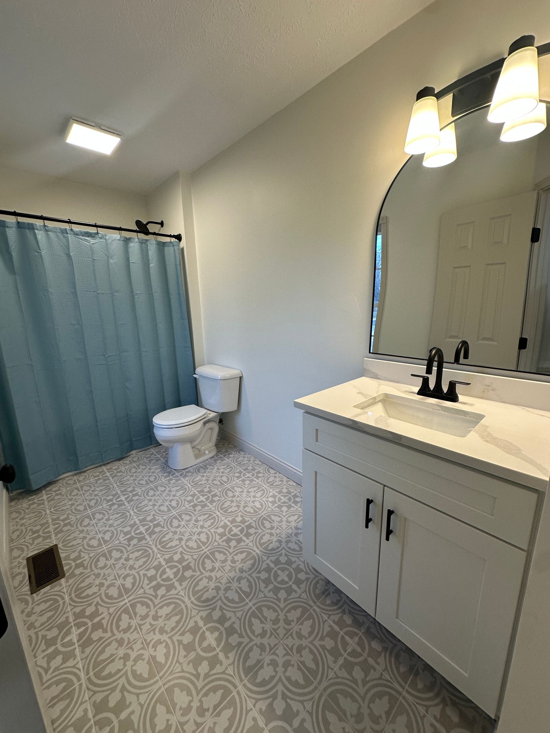 Bathroom with white vanity, patterned floor, blue shower curtain, toilet, and mirror.
