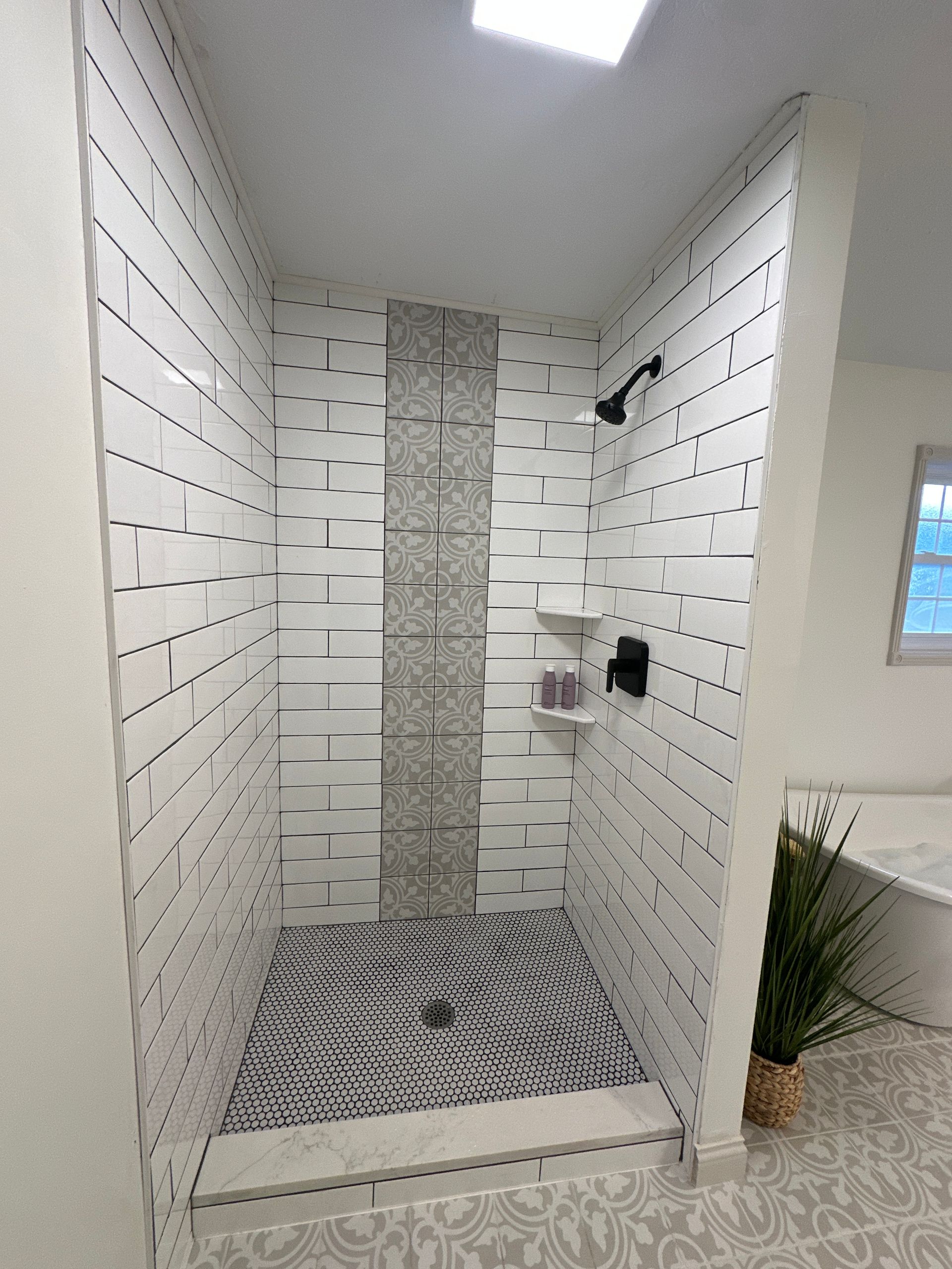 Modern shower with white, textured tile walls and a patterned mosaic floor.