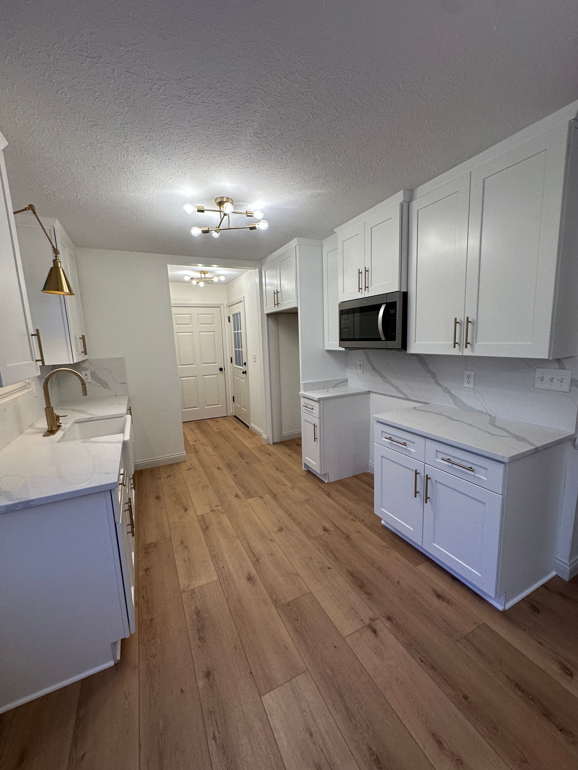 White kitchen with wood-look floors and cabinets, stainless steel appliances, and a doorway in the distance.