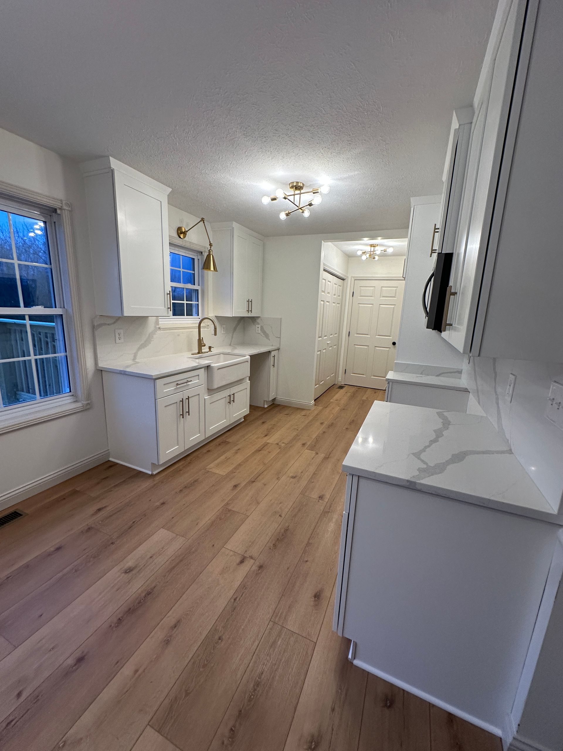 White kitchen with light wood floors, quartz countertops, and gold fixtures.