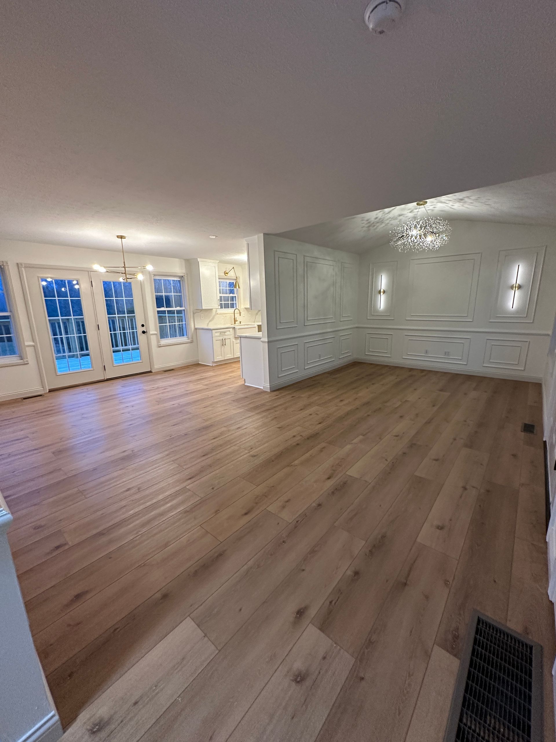 Empty living room with light wood floors, white walls and molding, and French doors.