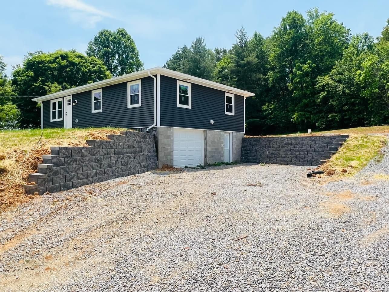 Dark blue house with white trim, a retaining wall, and gravel driveway.