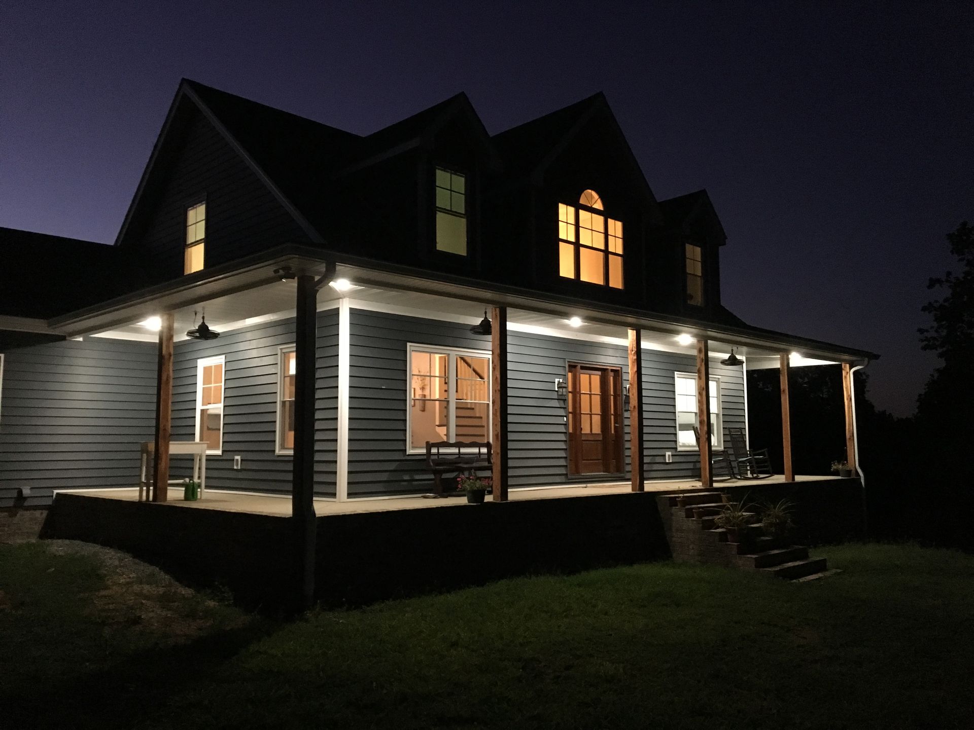Dark blue house at night with porch lights illuminating the front.
