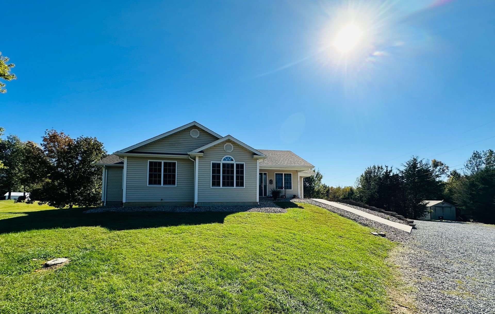 A ranch-style house on a sunny day with blue sky and a gravel driveway.