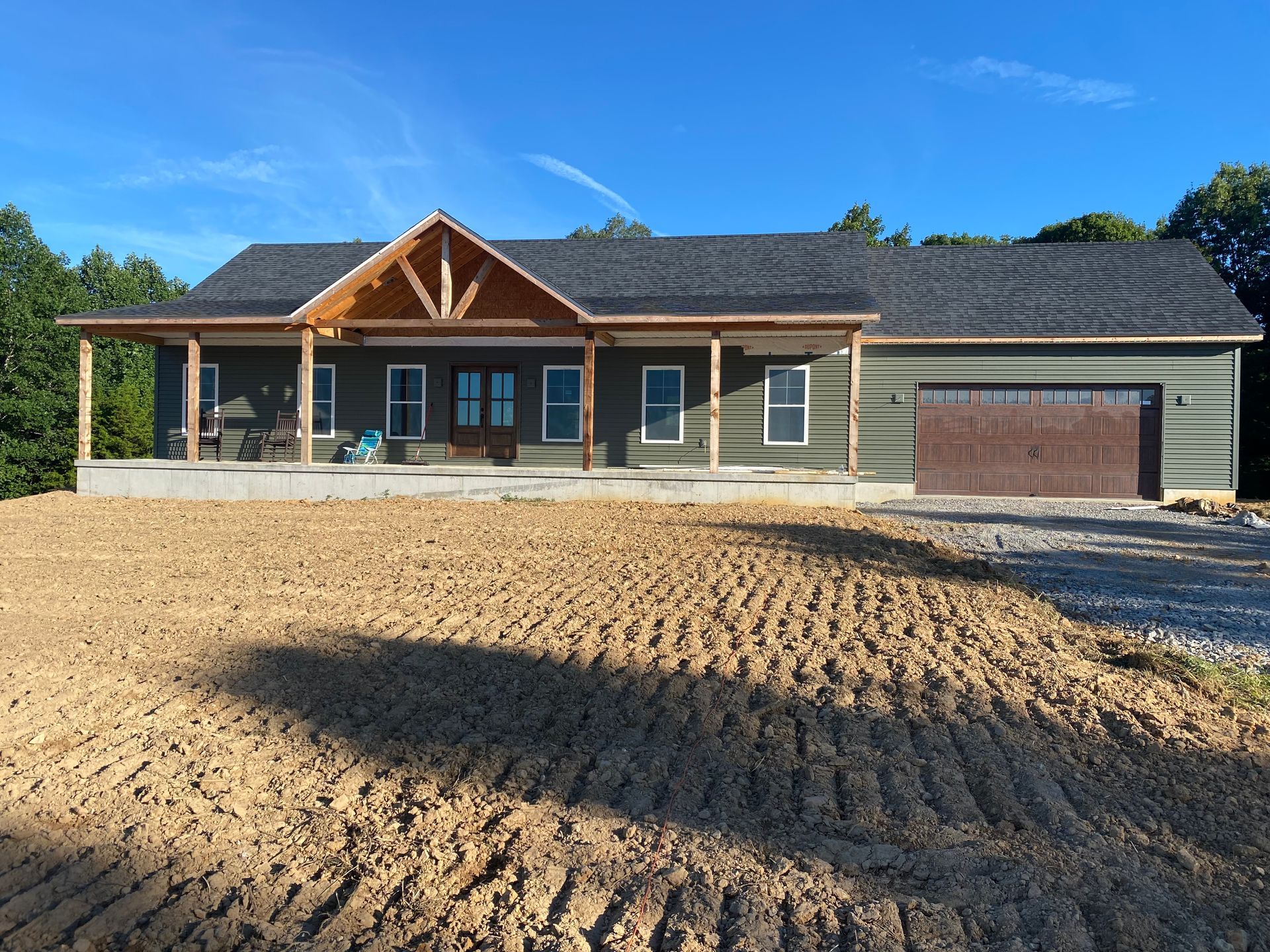 New house with a covered porch and brown garage door; unfinished yard.