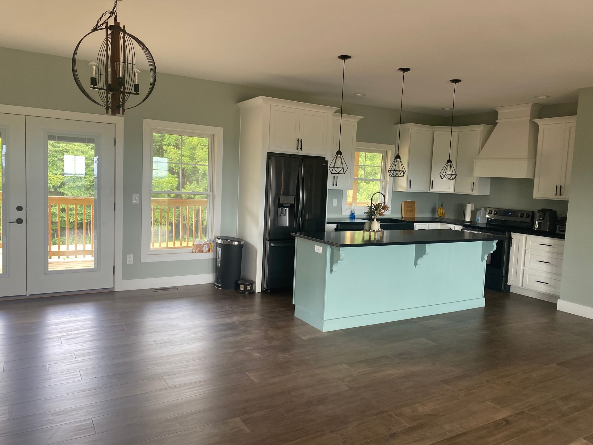 Spacious kitchen with white cabinets, teal island, dark appliances, and a wooden floor.