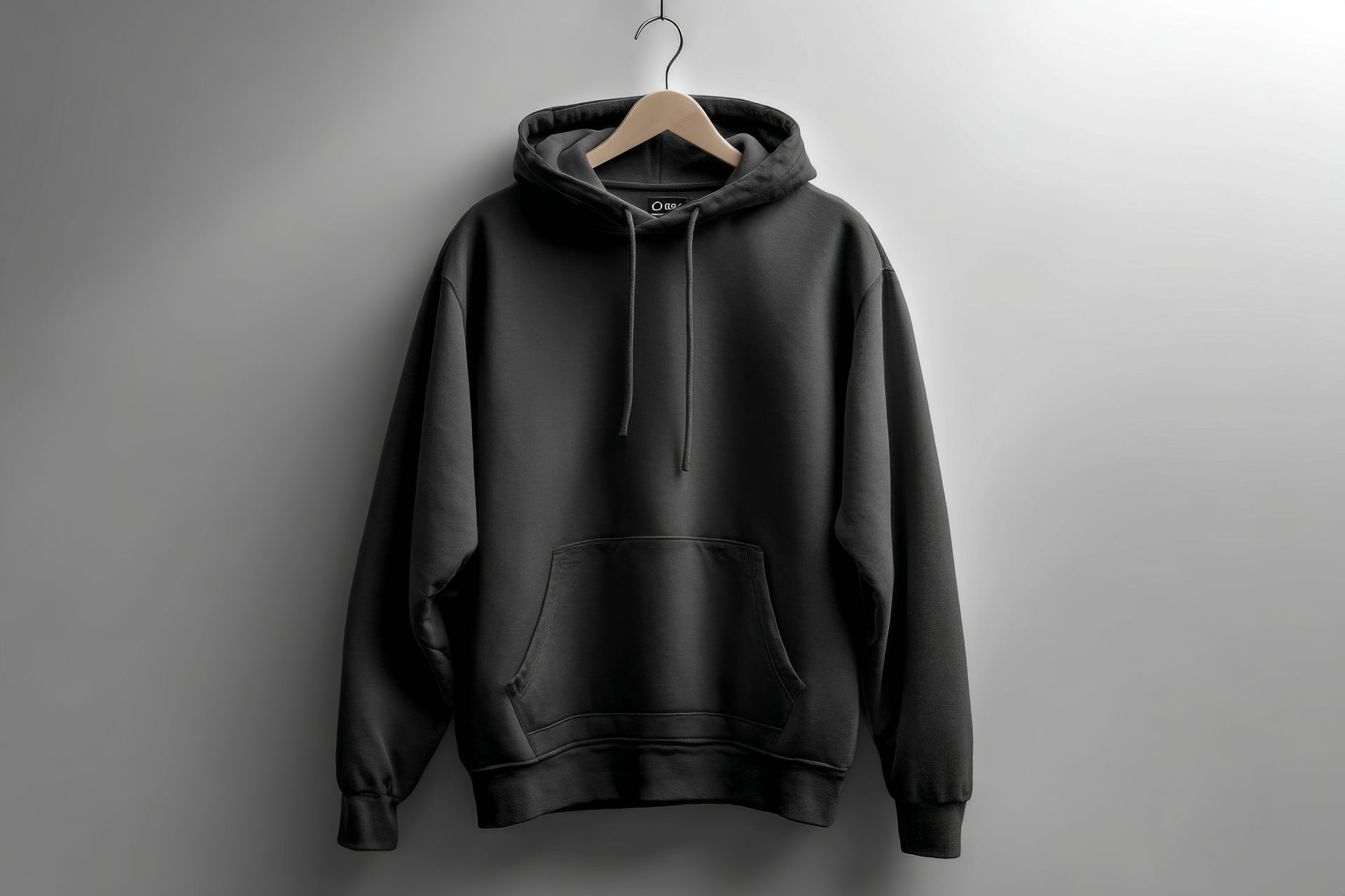 Black hoodie hanging on a wooden hanger against a gray wall.