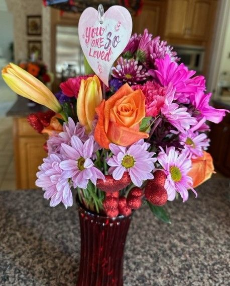 A vase filled with flowers and a heart that says you are so loved