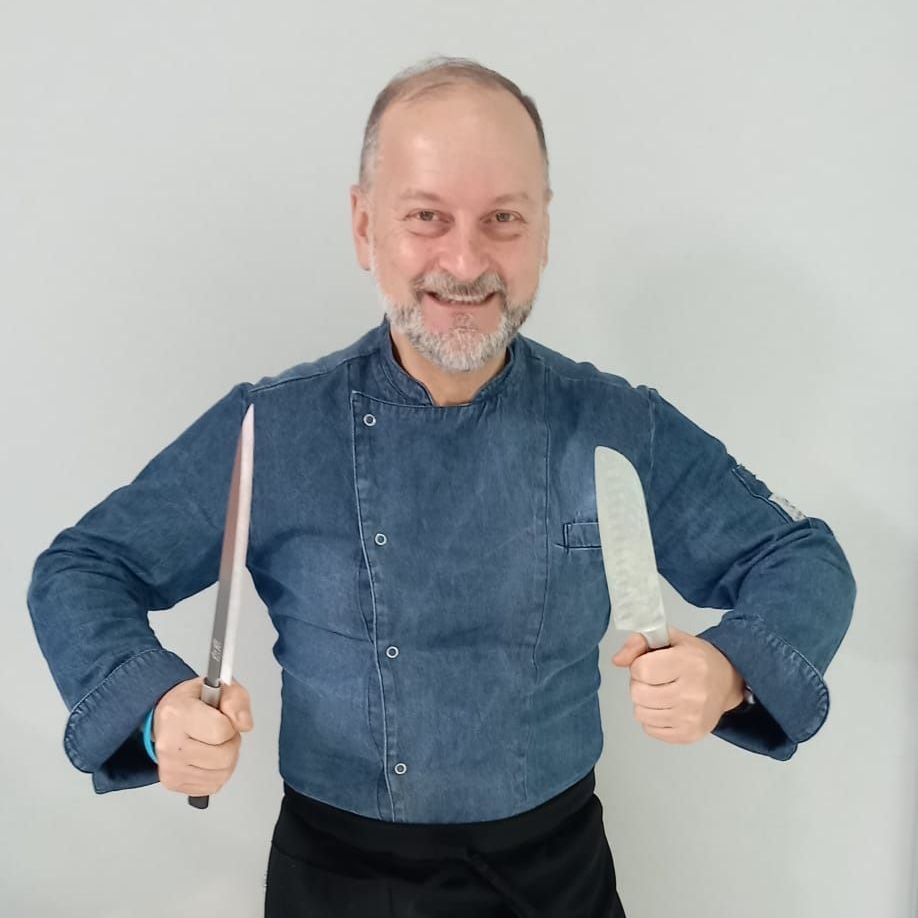 Un uomo con una camicia di jeans tiene in mano due coltelli