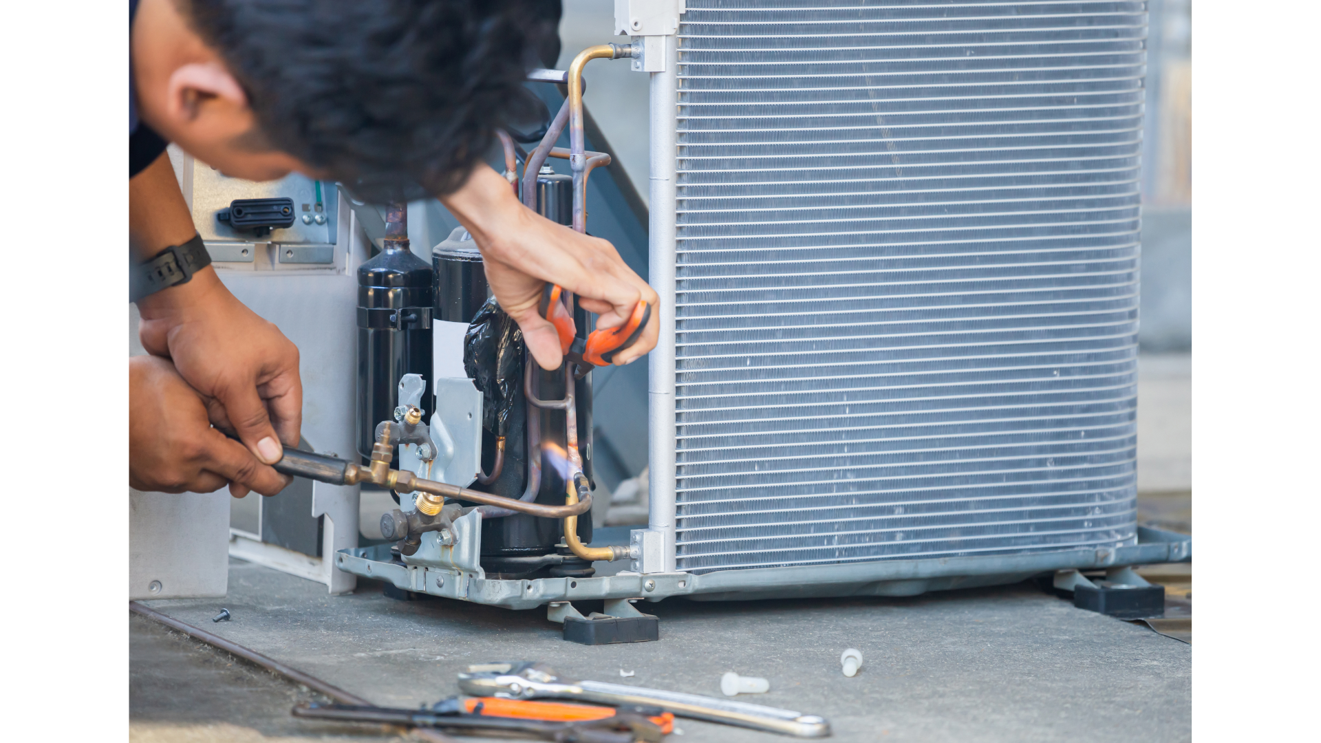 A man is fixing an air conditioner with a wrench.