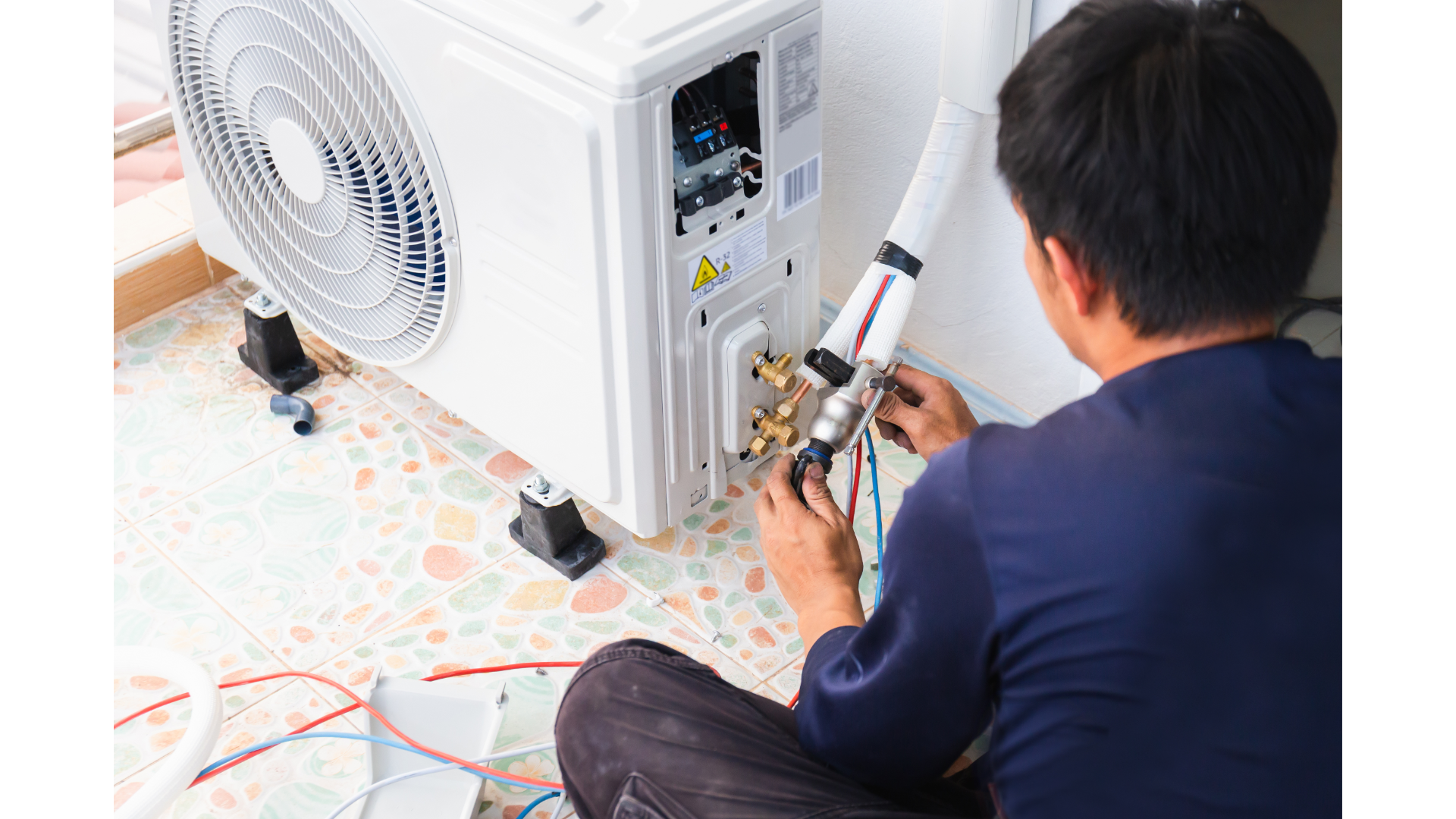 A man is sitting on the floor fixing an air conditioner.