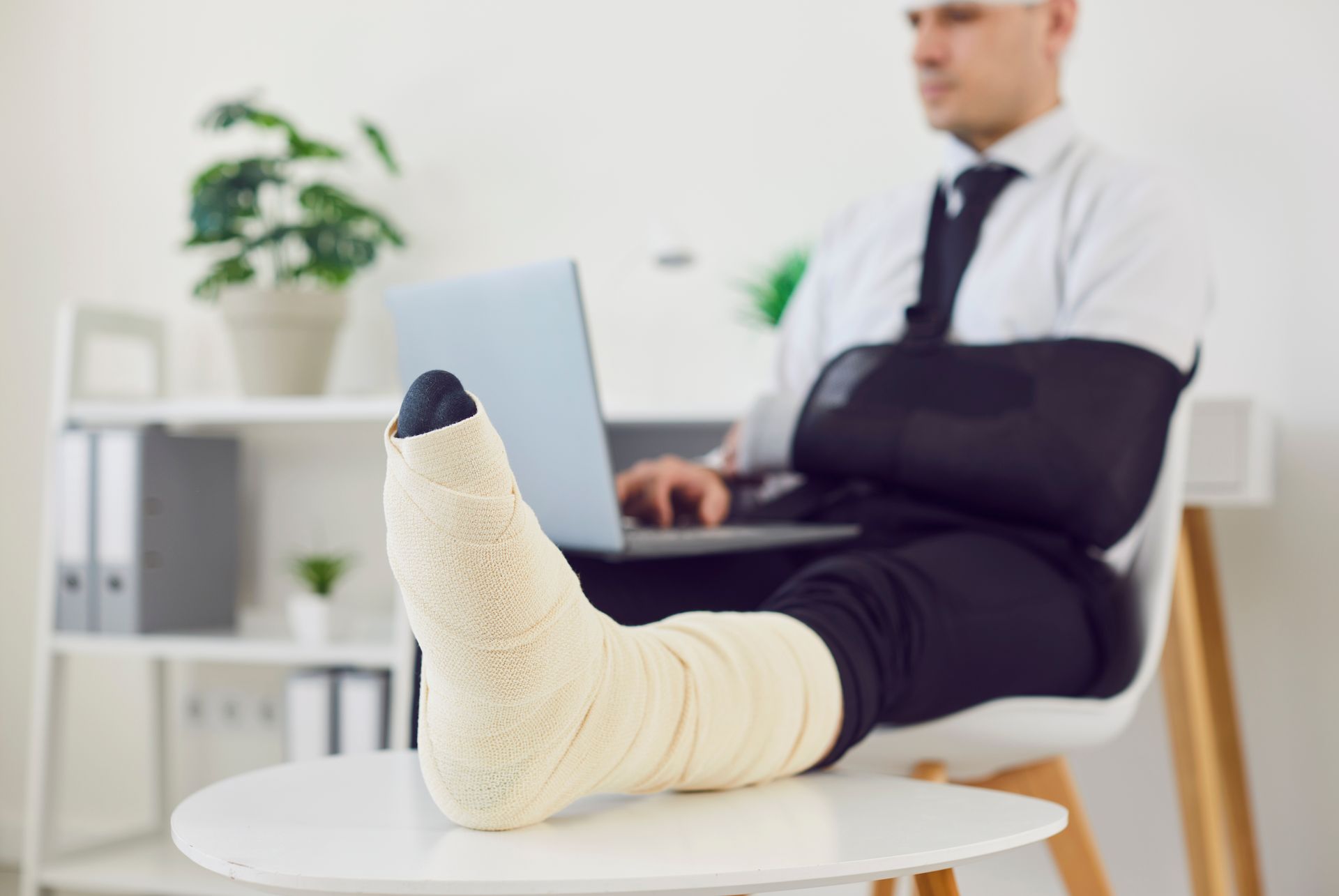 A man with a cast on his leg is using a laptop computer.