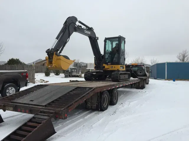 An excavator is sitting on top of a flatbed trailer in the snow.