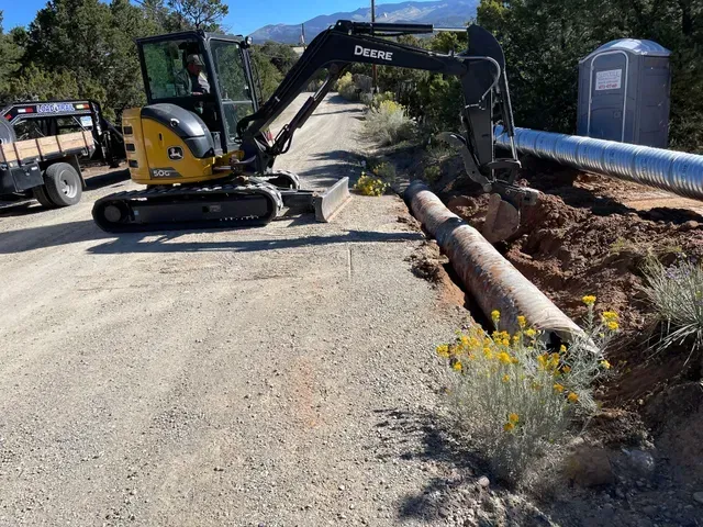 A john deere excavator is digging a hole in the ground next to a pipe.