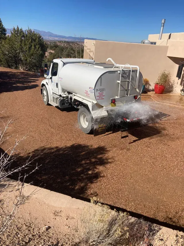 A white water truck is spraying water on a dirt road.