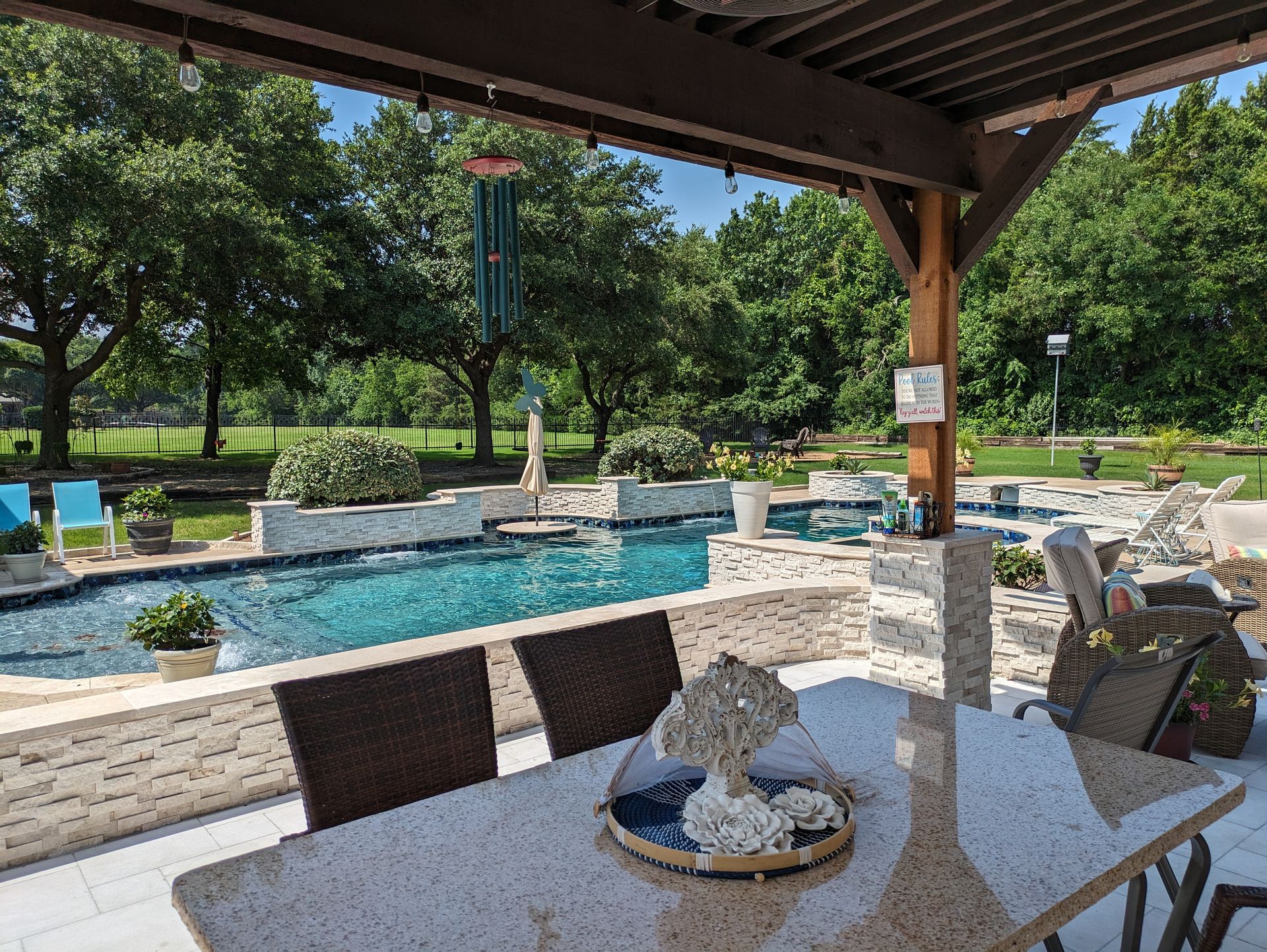A patio with a table and chairs and a pool in the background.
