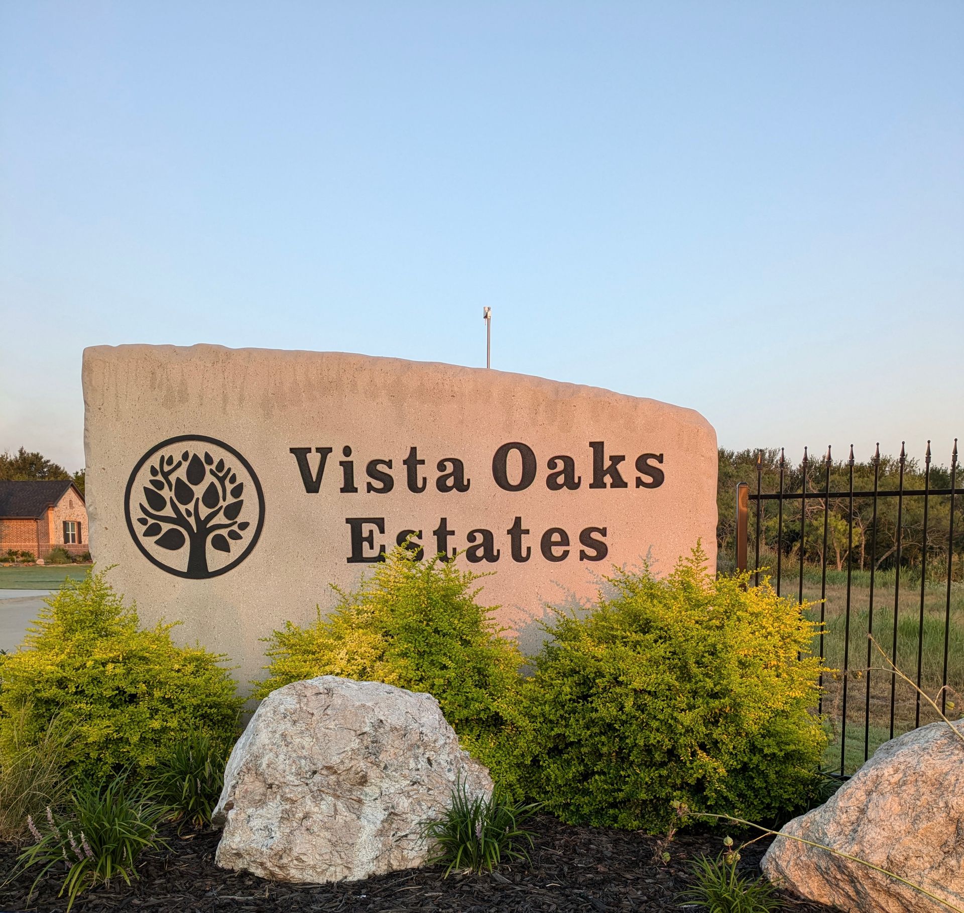 Sign for Vista Oaks Estates, carved in stone, with a tree logo, and landscaping.