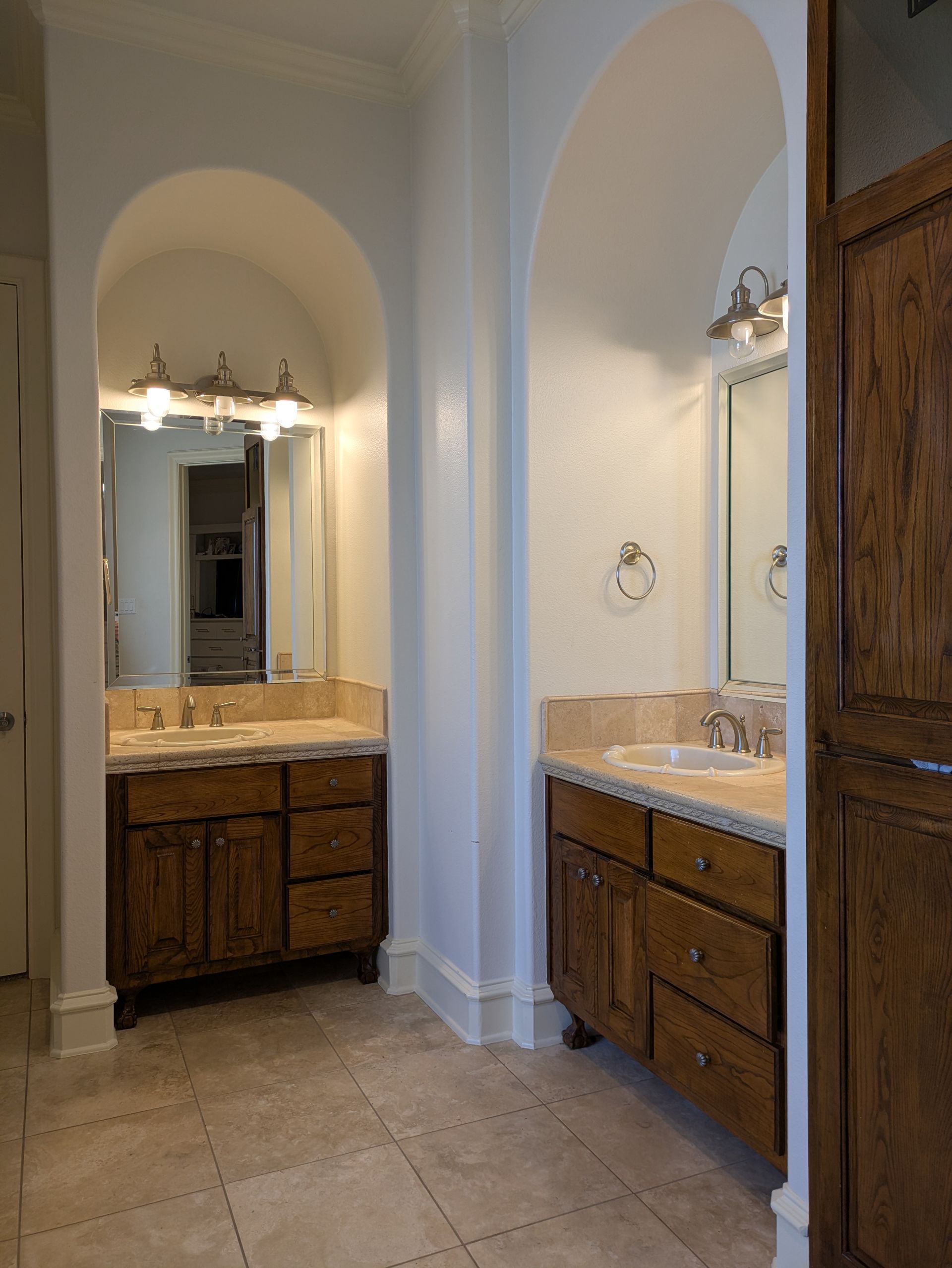 Two bathroom vanities in arched alcoves, with brown cabinets, granite countertops, and mirrors.