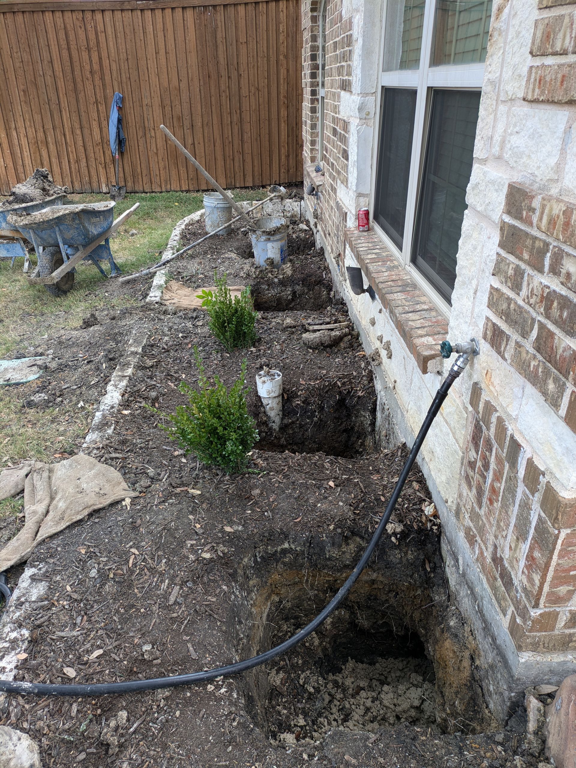 A hose is connected to a hole in the ground next to a brick building.