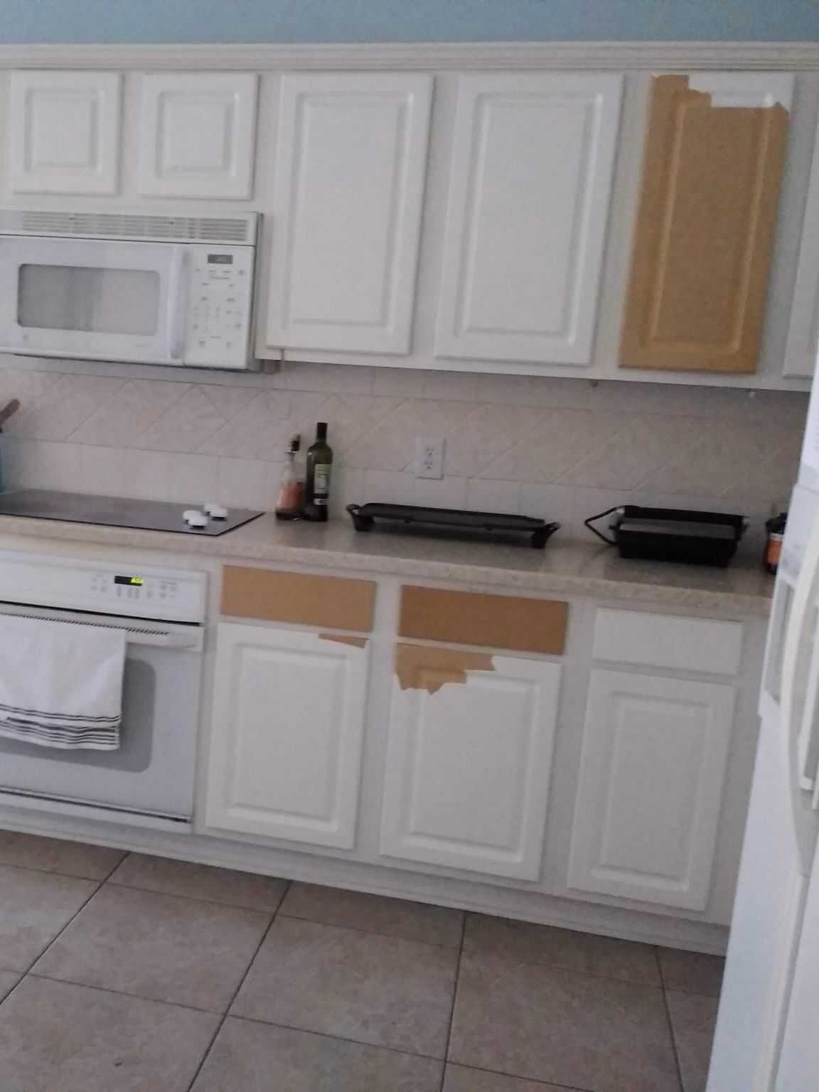 Kitchen cabinets, some painted white, with doors removed and showing bare wood, countertop, and appliances.