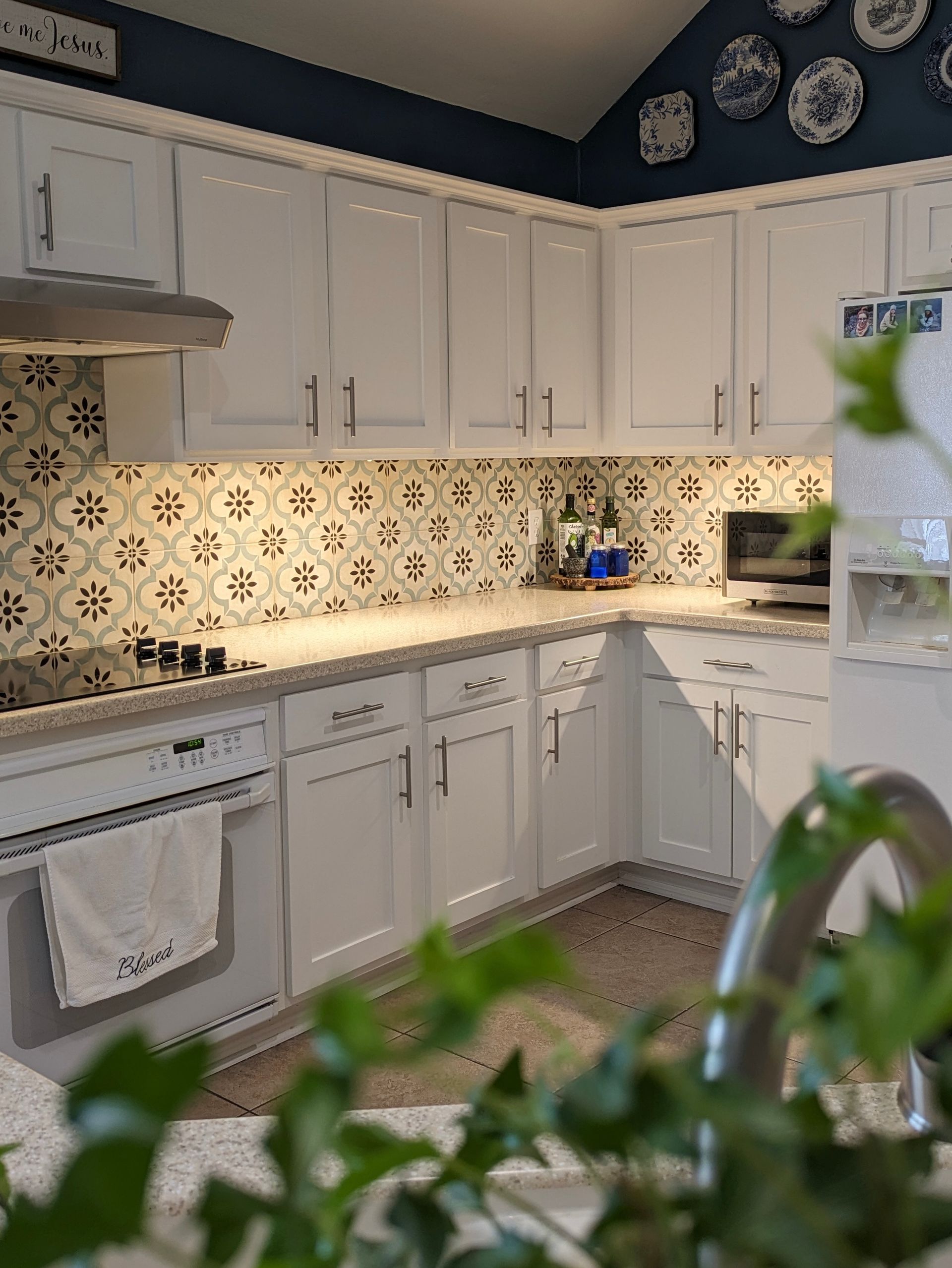 White kitchen with patterned backsplash, white countertops, and blue wall with decorative plates.