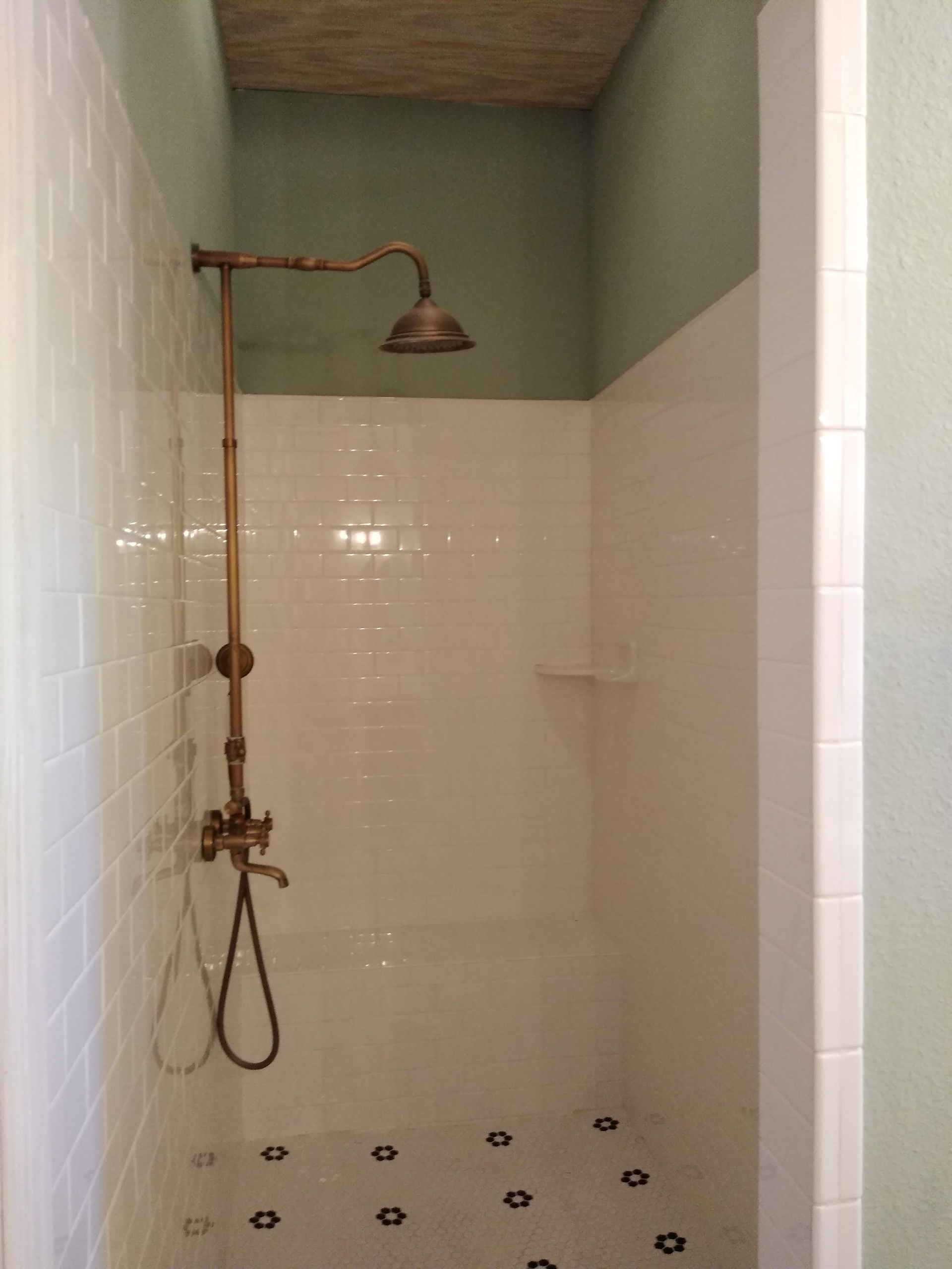 A shower with a brass shower head in a bathroom.