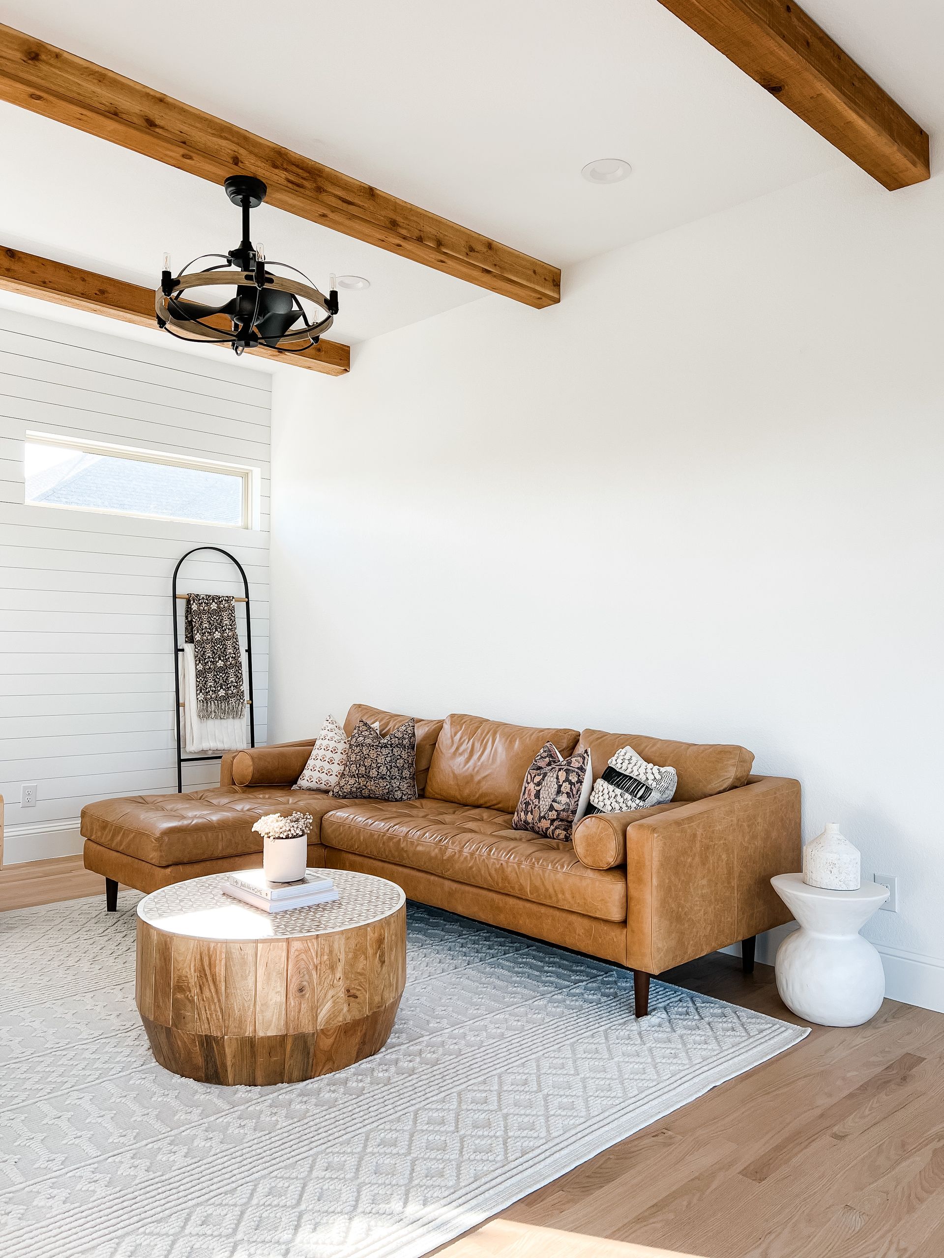 Living room with tan leather sectional sofa, wooden coffee table, and white rug.