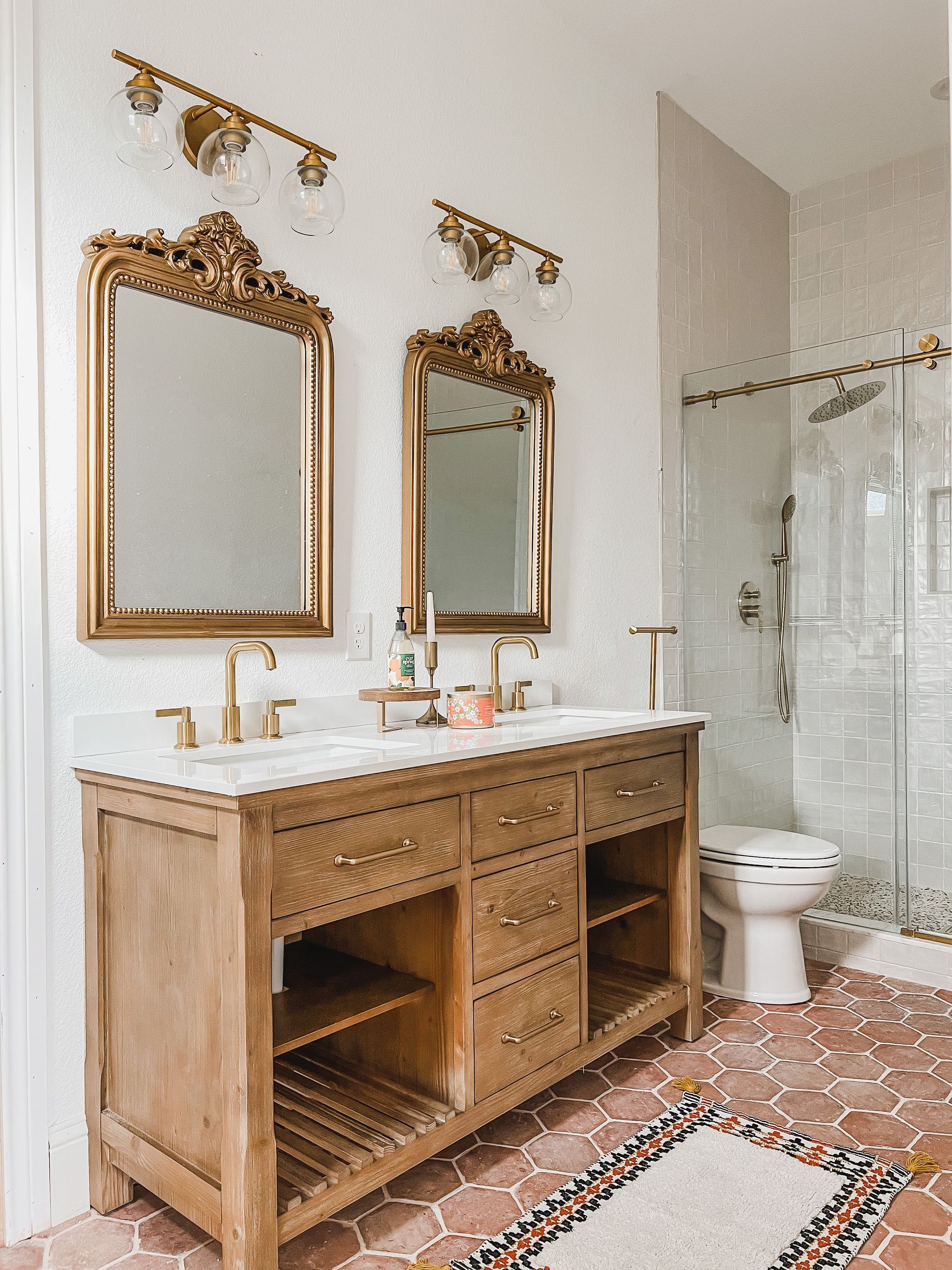 Bathroom with gold-framed mirrors, wooden vanity, and patterned tile floor.