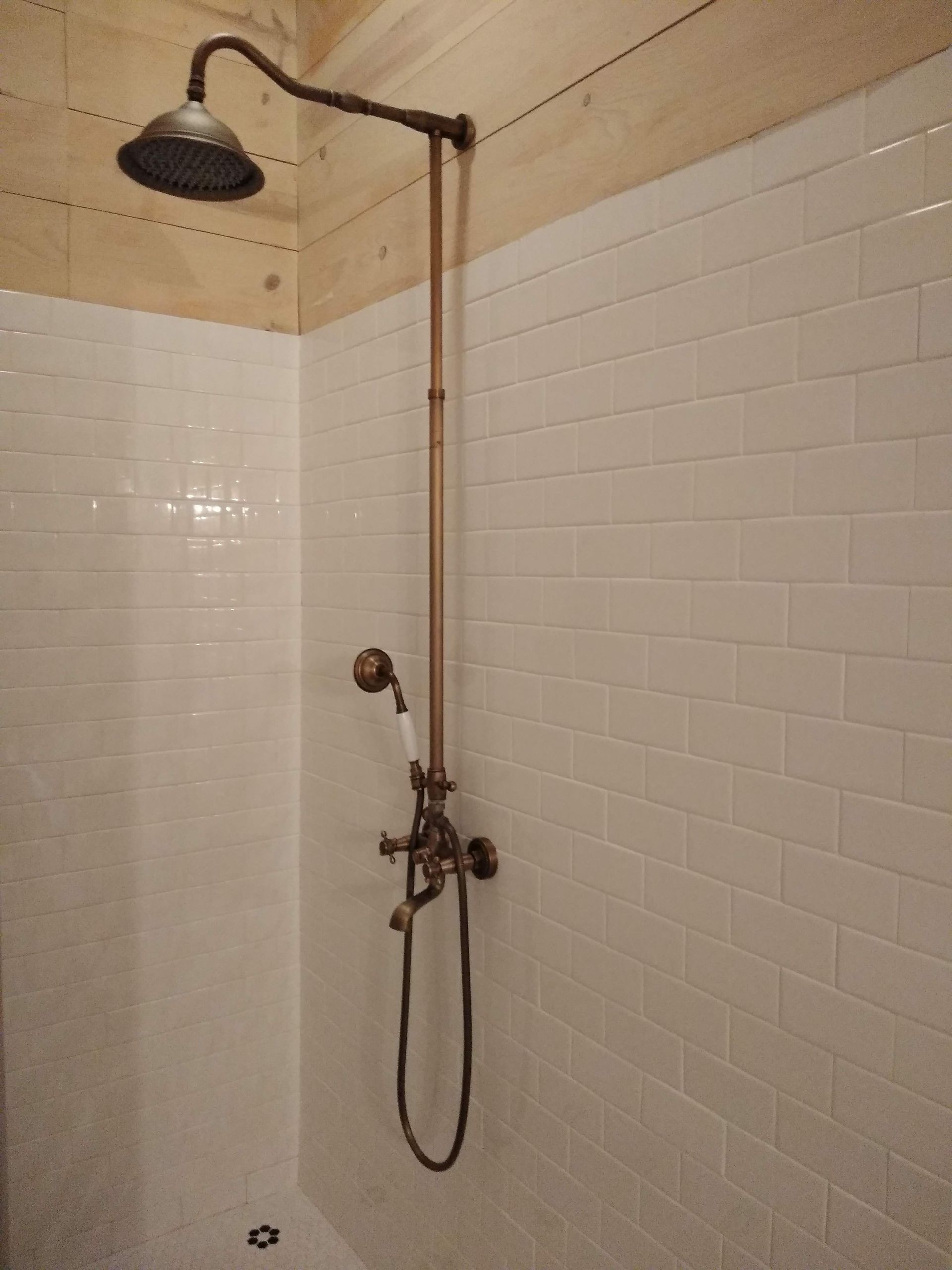 A shower with white tiles and a copper shower head