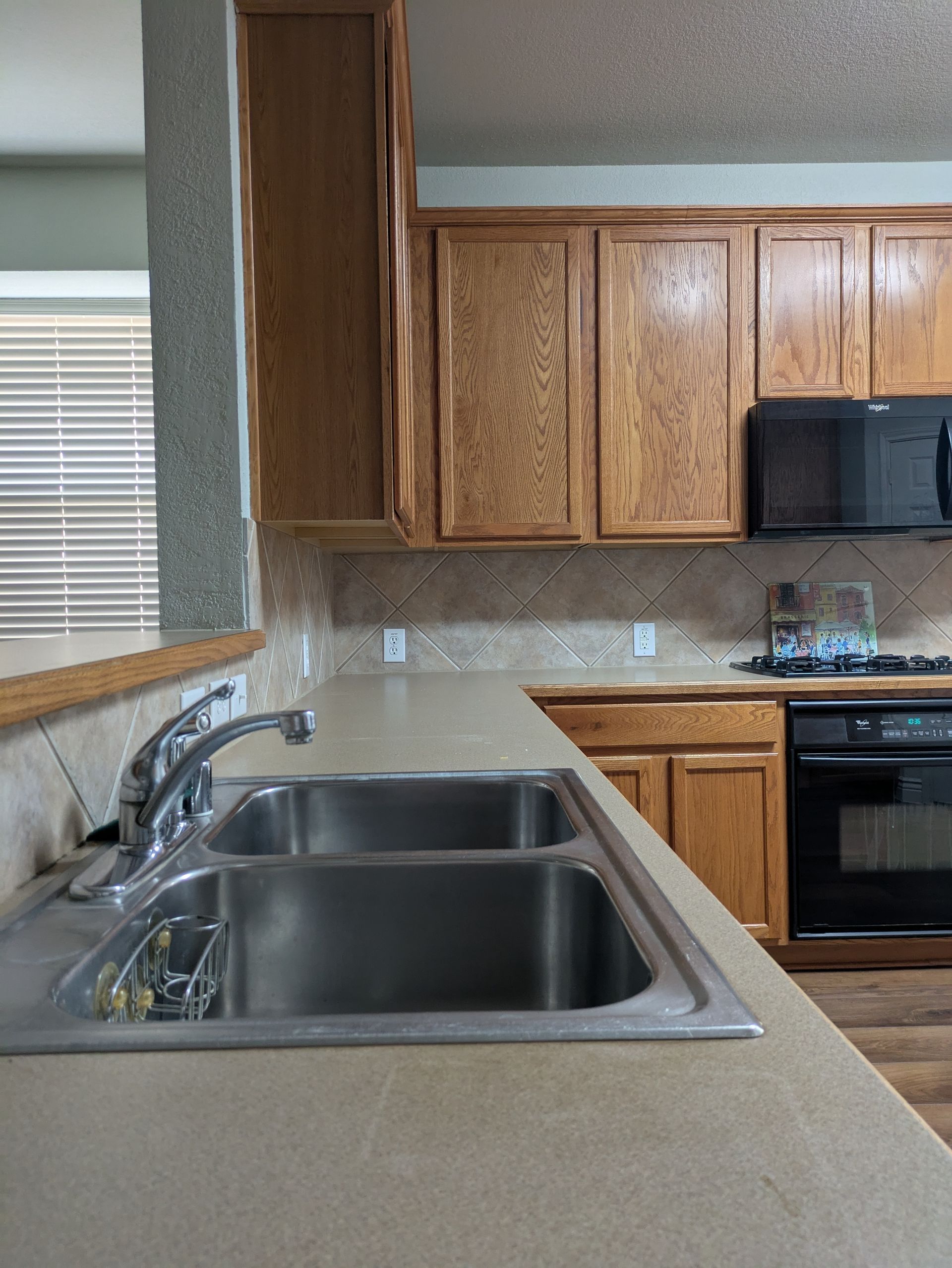 Kitchen with a stainless steel sink, light-colored countertops, wooden cabinets, and a black oven and microwave.