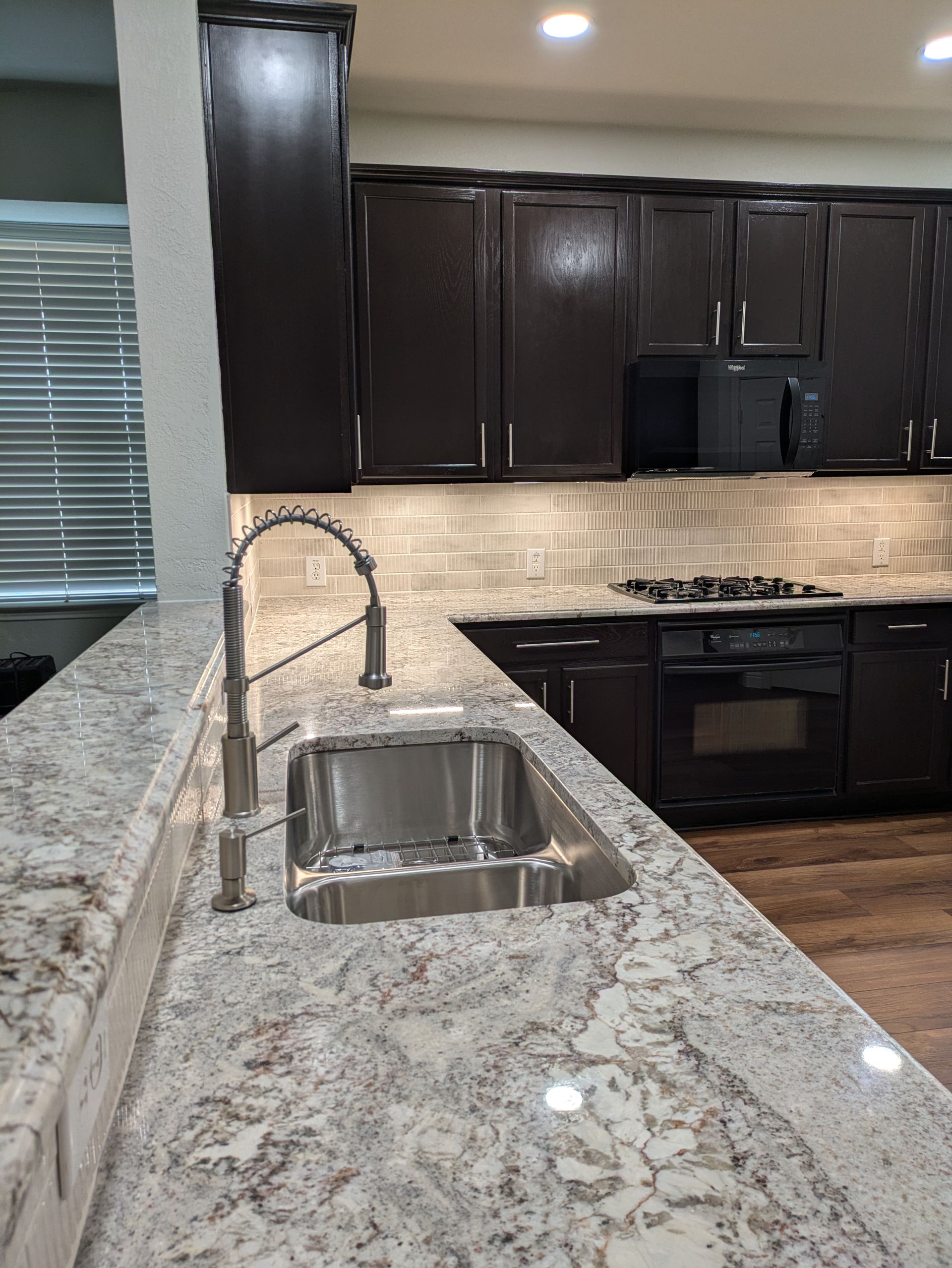 Kitchen with granite countertops, dark cabinets, stainless steel sink and faucet.
