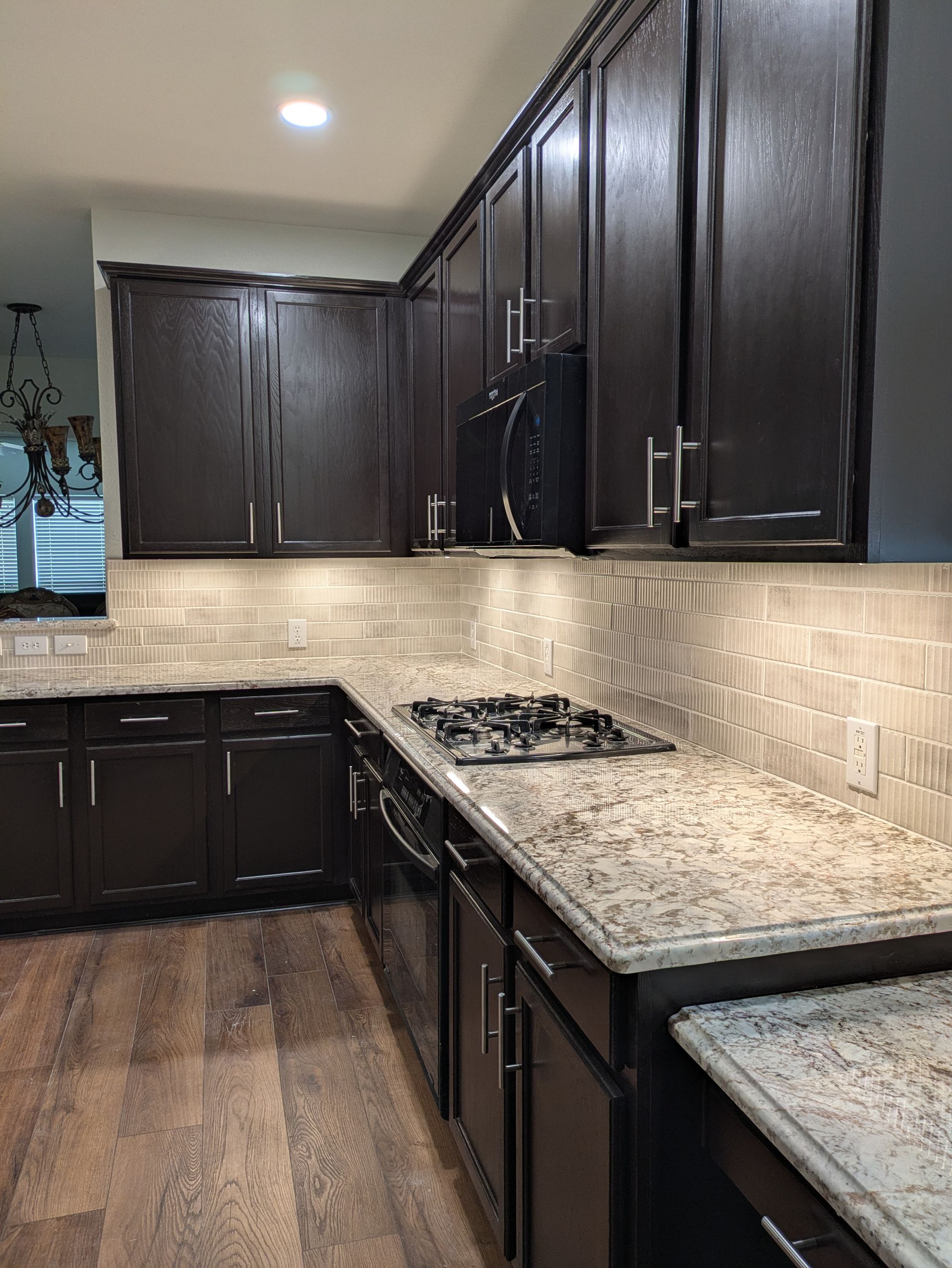 Dark brown kitchen cabinets, granite countertops, and tiled backsplash. Gas cooktop.