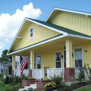 A yellow house with a green roof and an american flag on the porch.