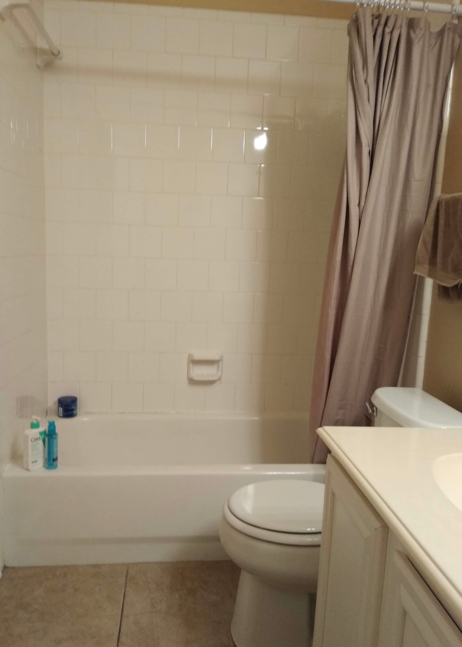 Bathroom with white tub, toilet, vanity, and shower curtain. Tile floor.